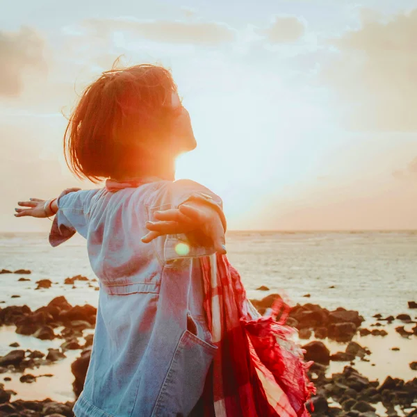 Femme paisible ouvrant les bras vers l'océan au soleil levant